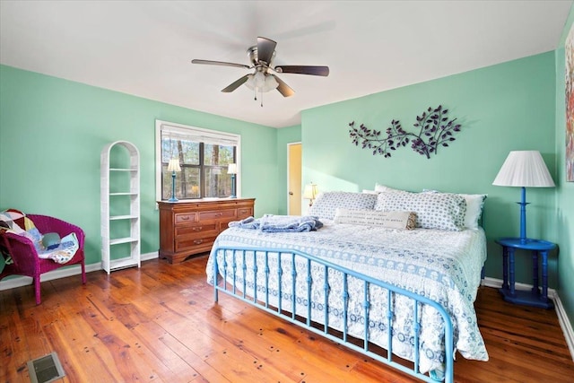 bedroom featuring a ceiling fan, visible vents, baseboards, and wood finished floors