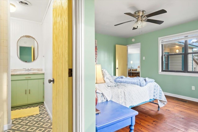 bedroom with baseboards, visible vents, a sink, and wood finished floors