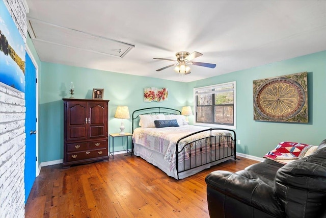 bedroom featuring a ceiling fan, attic access, baseboards, and wood finished floors