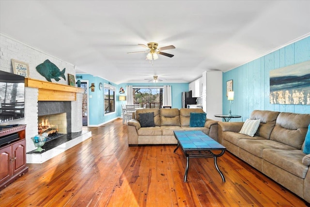 living area featuring ceiling fan, ornamental molding, a brick fireplace, and wood finished floors