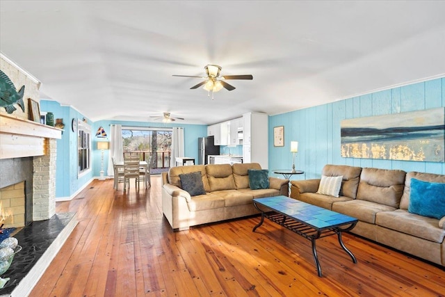 living room featuring ceiling fan, a brick fireplace, and wood finished floors