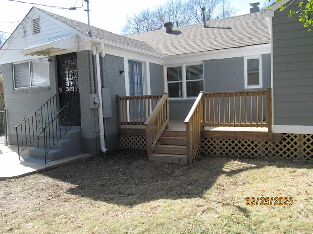 back of property featuring brick siding, a lawn, and roof with shingles