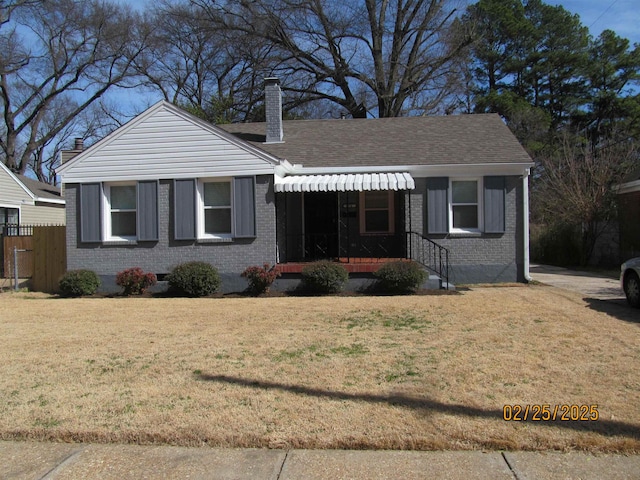 view of front of property featuring a shingled roof, brick siding, a chimney, and a front lawn