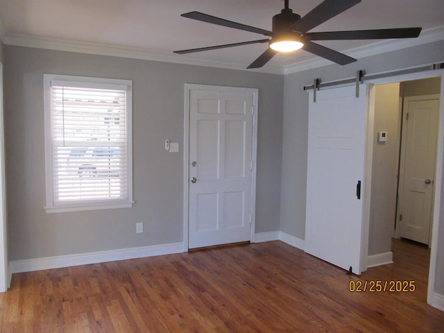 empty room featuring a barn door, dark wood-type flooring, and crown molding