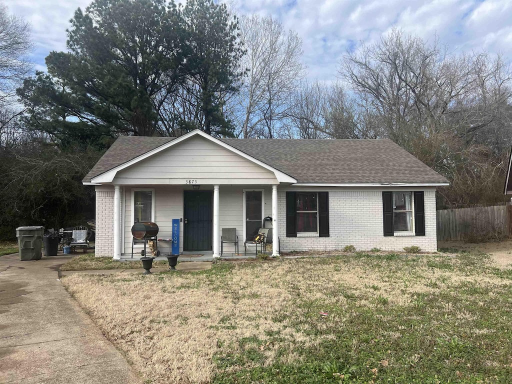 ranch-style home with covered porch, brick siding, fence, roof with shingles, and a front lawn