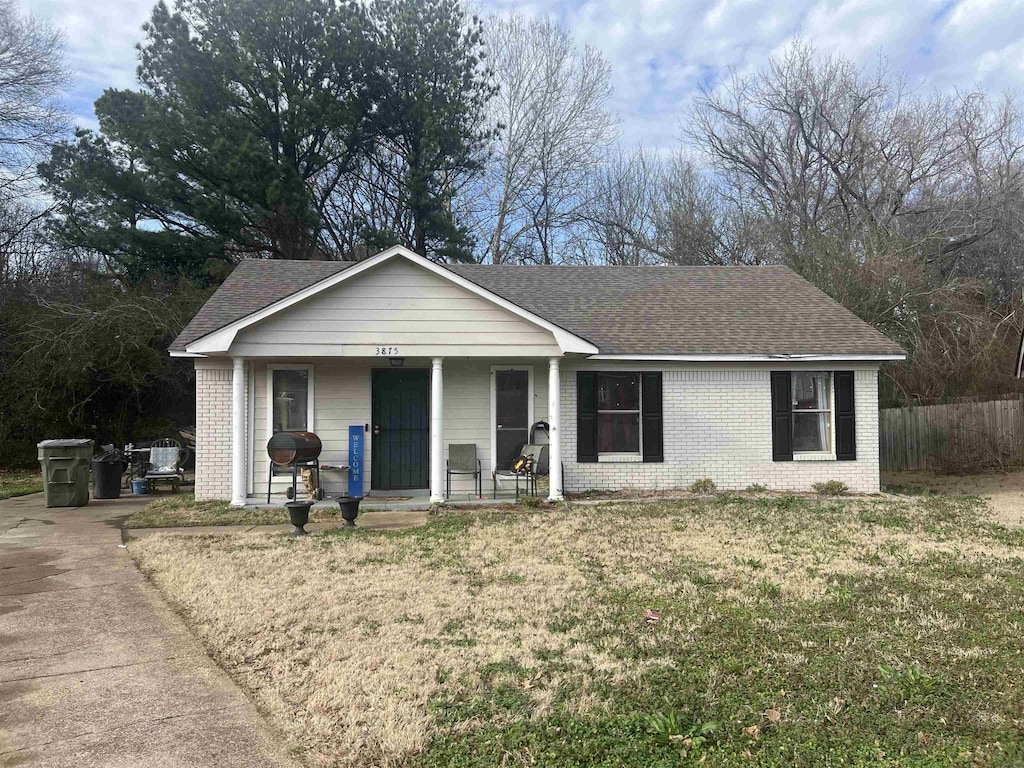 ranch-style house featuring covered porch, roof with shingles, a front yard, and brick siding