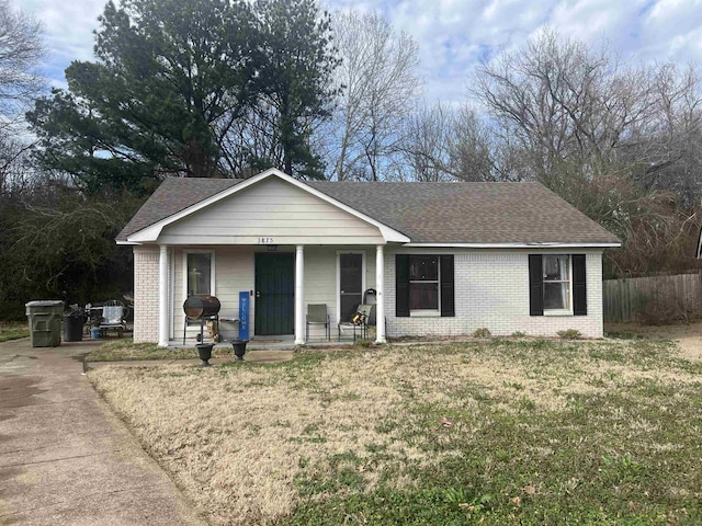 ranch-style house featuring covered porch, roof with shingles, a front yard, and brick siding