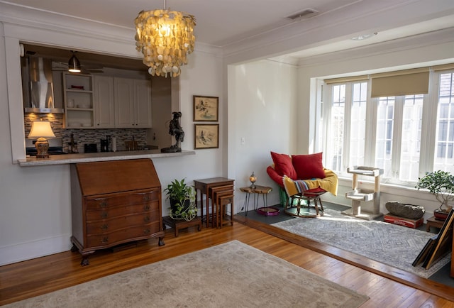 sitting room with baseboards, visible vents, wood finished floors, crown molding, and a notable chandelier