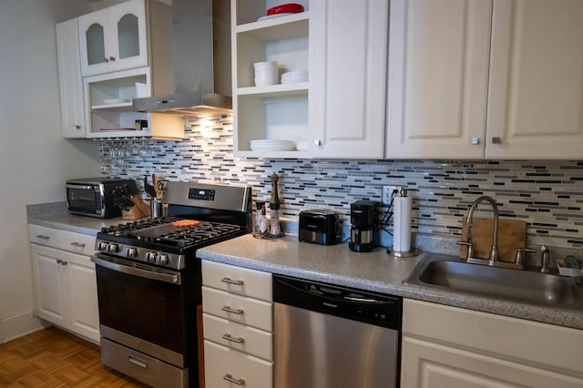 kitchen featuring decorative backsplash, appliances with stainless steel finishes, white cabinetry, a sink, and wall chimney exhaust hood