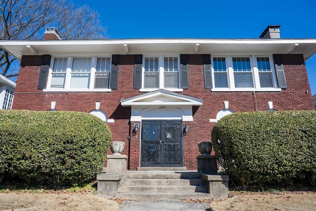 view of front of house featuring entry steps, brick siding, and a chimney