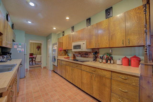 kitchen featuring brick floor, stainless steel appliances, recessed lighting, light countertops, and a textured ceiling