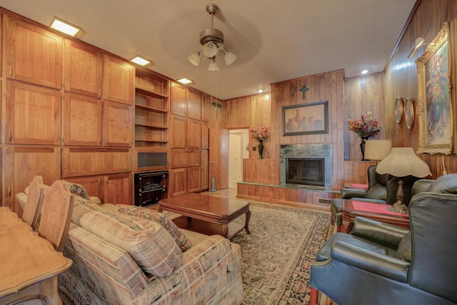 living area featuring built in shelves, a fireplace, wooden walls, and ceiling fan