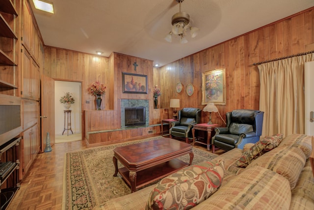 living room with a textured ceiling, wooden walls, a fireplace with raised hearth, and a ceiling fan