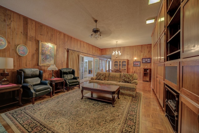 living room with wood walls, a textured ceiling, and ceiling fan with notable chandelier