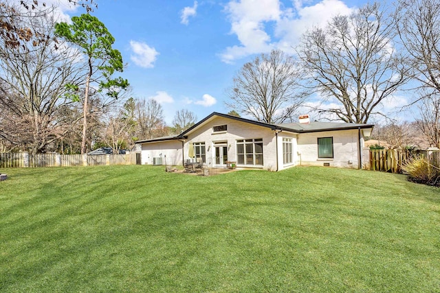 back of property with a chimney, a fenced backyard, and a lawn