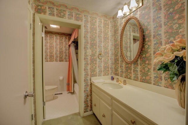 bathroom with a textured ceiling, toilet, a wainscoted wall, tile walls, and wallpapered walls