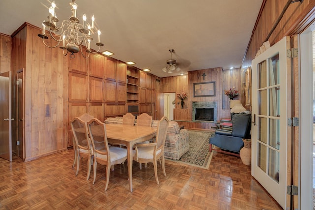 dining space with a fireplace, wooden walls, baseboards, and ceiling fan with notable chandelier