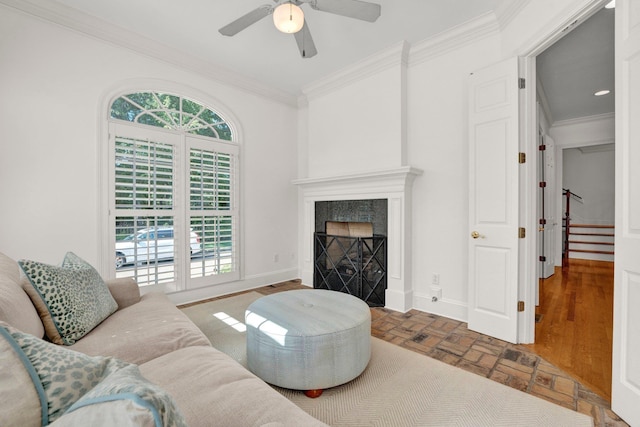 living room featuring a ceiling fan, a high end fireplace, crown molding, and baseboards