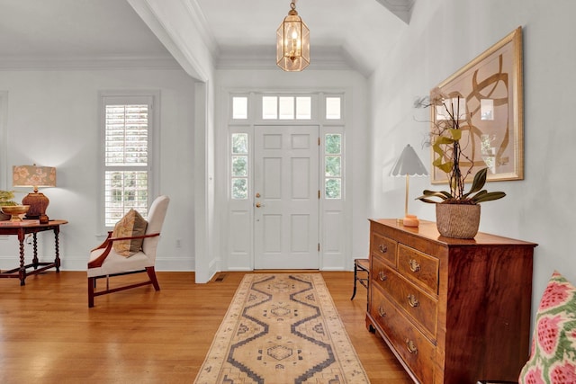 foyer with light wood finished floors, baseboards, ornamental molding, and a chandelier