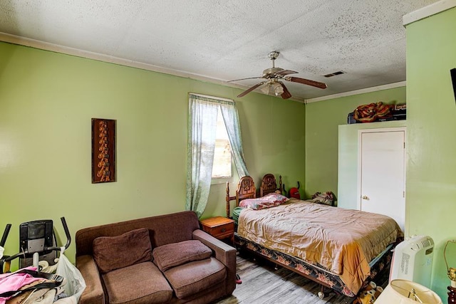 bedroom with a textured ceiling, ceiling fan, wood finished floors, visible vents, and ornamental molding