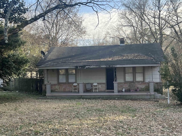 back of property with stone siding, a porch, and a lawn