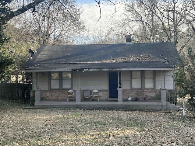 view of front of home with a shingled roof, stone siding, covered porch, and a chimney