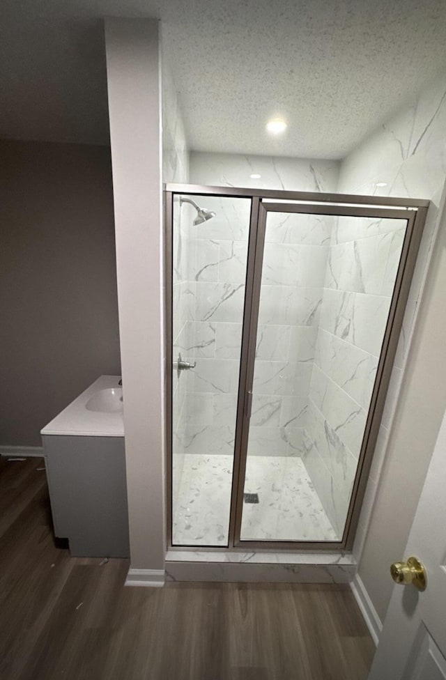 bathroom featuring baseboards, a textured ceiling, a marble finish shower, and wood finished floors