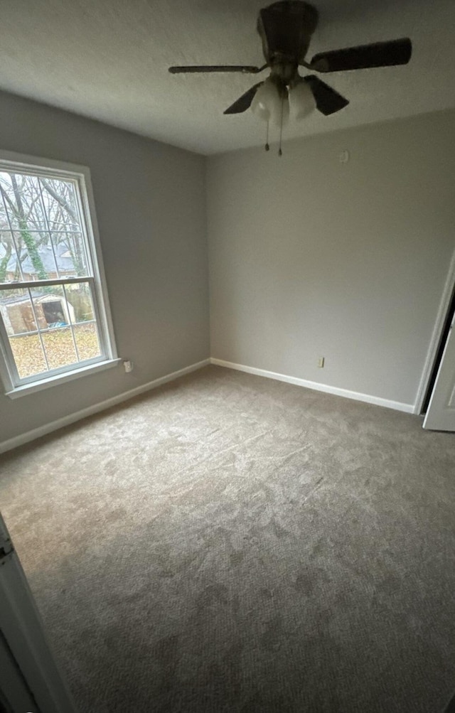 carpeted spare room featuring baseboards and a ceiling fan