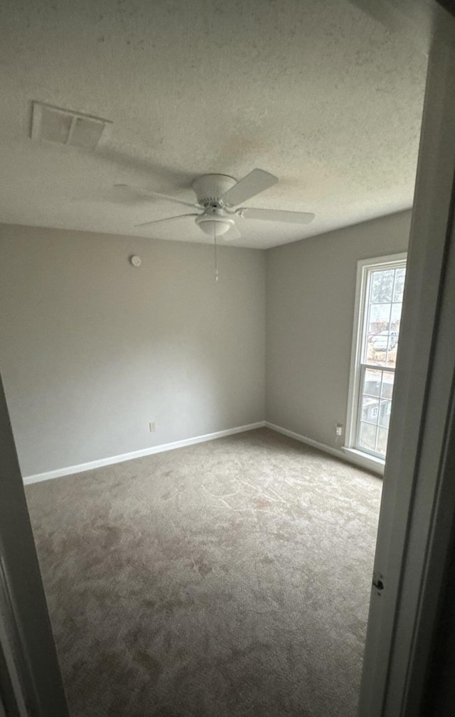 empty room featuring a textured ceiling, carpet flooring, visible vents, and baseboards