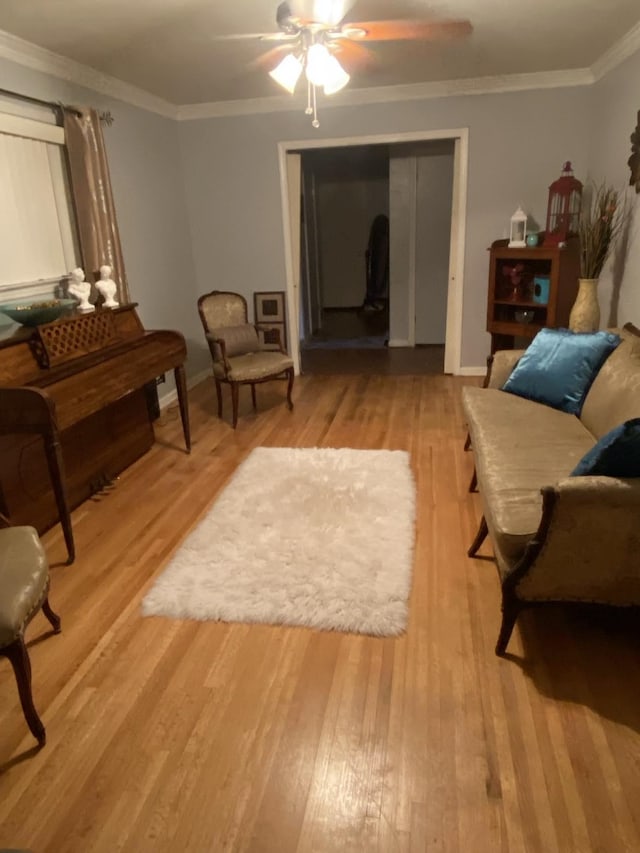 sitting room with light wood-type flooring, baseboards, a ceiling fan, and crown molding