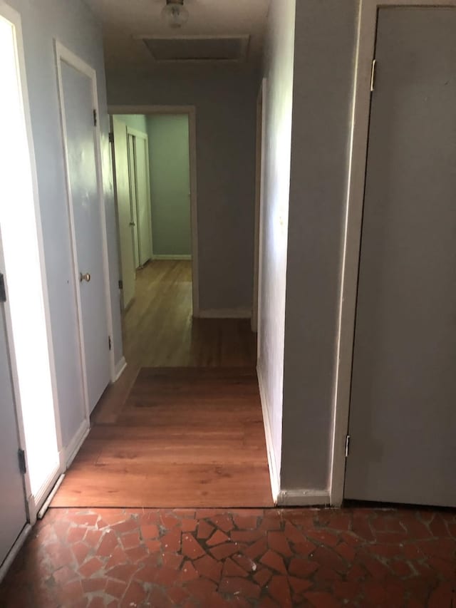 hallway featuring wood finished floors, attic access, and baseboards