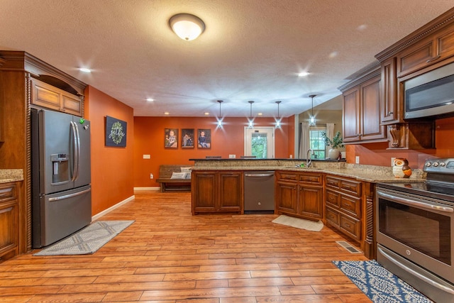 kitchen featuring appliances with stainless steel finishes, brown cabinets, decorative light fixtures, a peninsula, and a sink