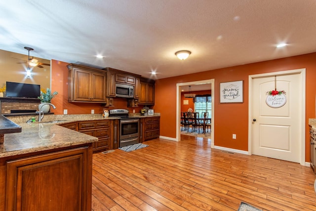 kitchen featuring brown cabinets, appliances with stainless steel finishes, a sink, light wood-type flooring, and a peninsula