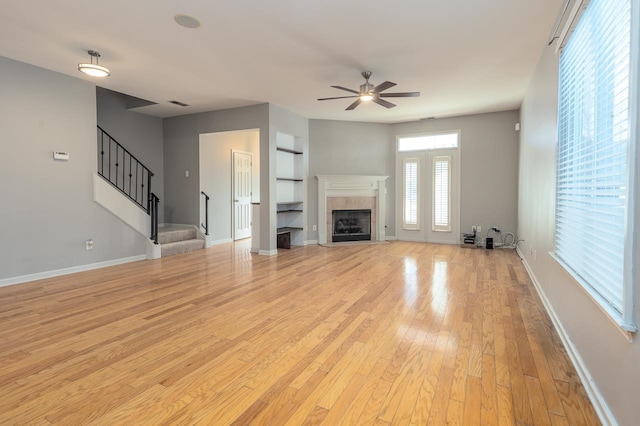 unfurnished living room with a fireplace, a ceiling fan, baseboards, stairs, and light wood finished floors