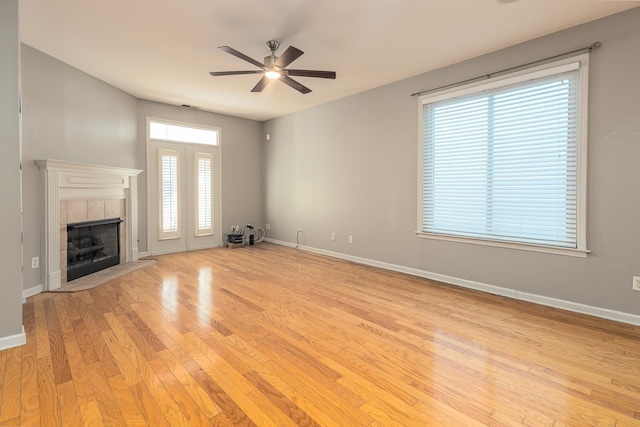 unfurnished living room featuring light wood-type flooring, ceiling fan, baseboards, and a tile fireplace