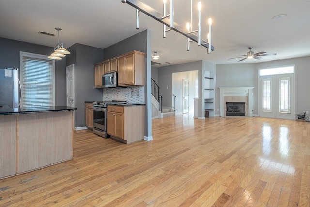 kitchen with light wood-style flooring, stainless steel appliances, a fireplace, visible vents, and dark countertops