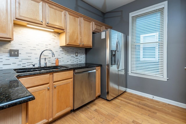 kitchen with tasteful backsplash, appliances with stainless steel finishes, dark stone countertops, light wood-style floors, and a sink