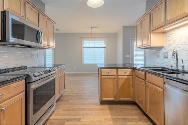 kitchen featuring appliances with stainless steel finishes, dark stone countertops, a peninsula, light wood-style floors, and a sink