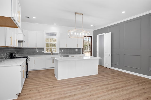 kitchen with a kitchen island, appliances with stainless steel finishes, hanging light fixtures, white cabinetry, and a decorative wall