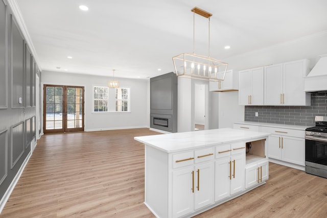 kitchen with open floor plan, stainless steel gas range oven, white cabinetry, and decorative light fixtures