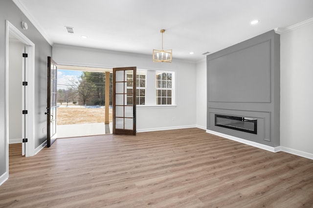 unfurnished living room featuring wood finished floors, ornamental molding, a glass covered fireplace, and visible vents