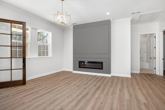 unfurnished living room featuring a fireplace, visible vents, attic access, ornamental molding, and light wood-type flooring