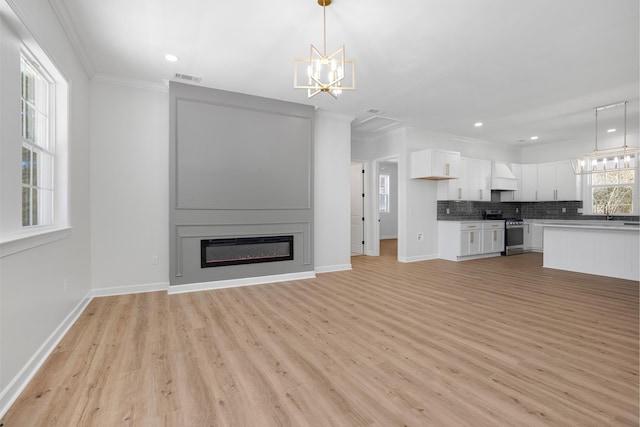 unfurnished living room with light wood finished floors, visible vents, a glass covered fireplace, crown molding, and a notable chandelier