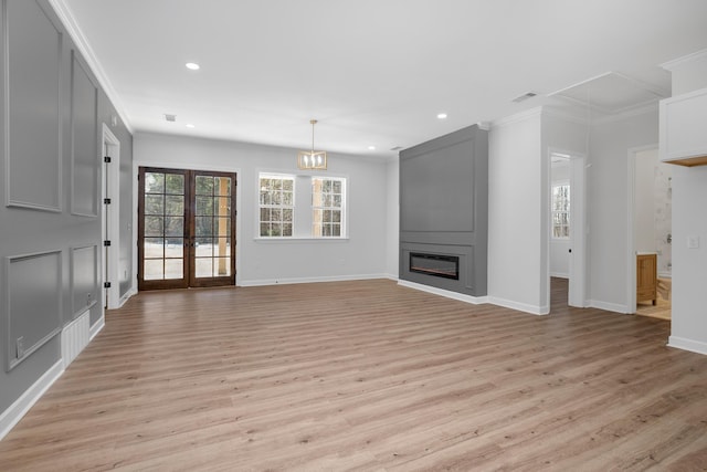 unfurnished living room featuring a large fireplace, ornamental molding, light wood-style flooring, and attic access