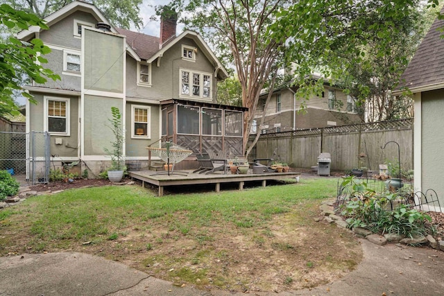 back of property with a deck, a chimney, a fenced backyard, and a sunroom