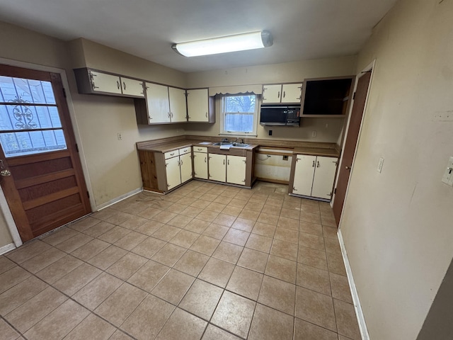 kitchen with light tile patterned floors, baseboards, black microwave, and white cabinets