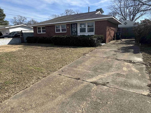 ranch-style home featuring driveway, brick siding, a front lawn, and fence