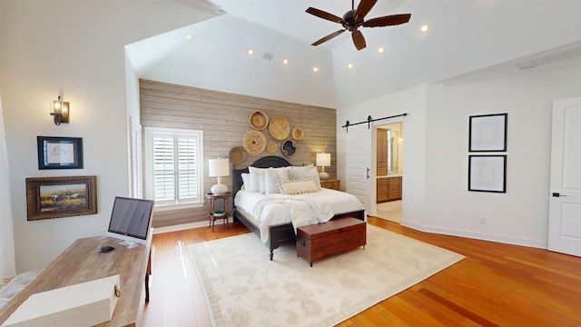 bedroom featuring a barn door, baseboards, ensuite bath, light wood-type flooring, and recessed lighting