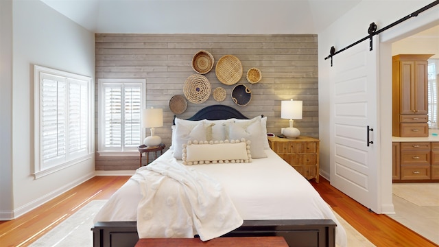 bedroom featuring light wood-type flooring, baseboards, and a barn door