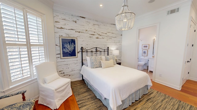 bedroom with connected bathroom, an accent wall, dark wood-style flooring, visible vents, and ornamental molding